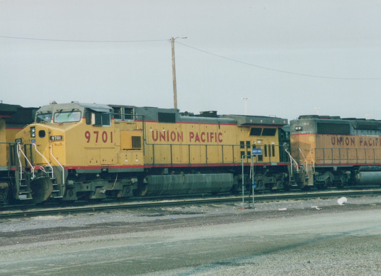 Two large yellow Union Pacific diesel locomotives, numbered 9701 and 3810, sit parked side-by-side on parallel tracks in a gravel yard on a cloudy day.