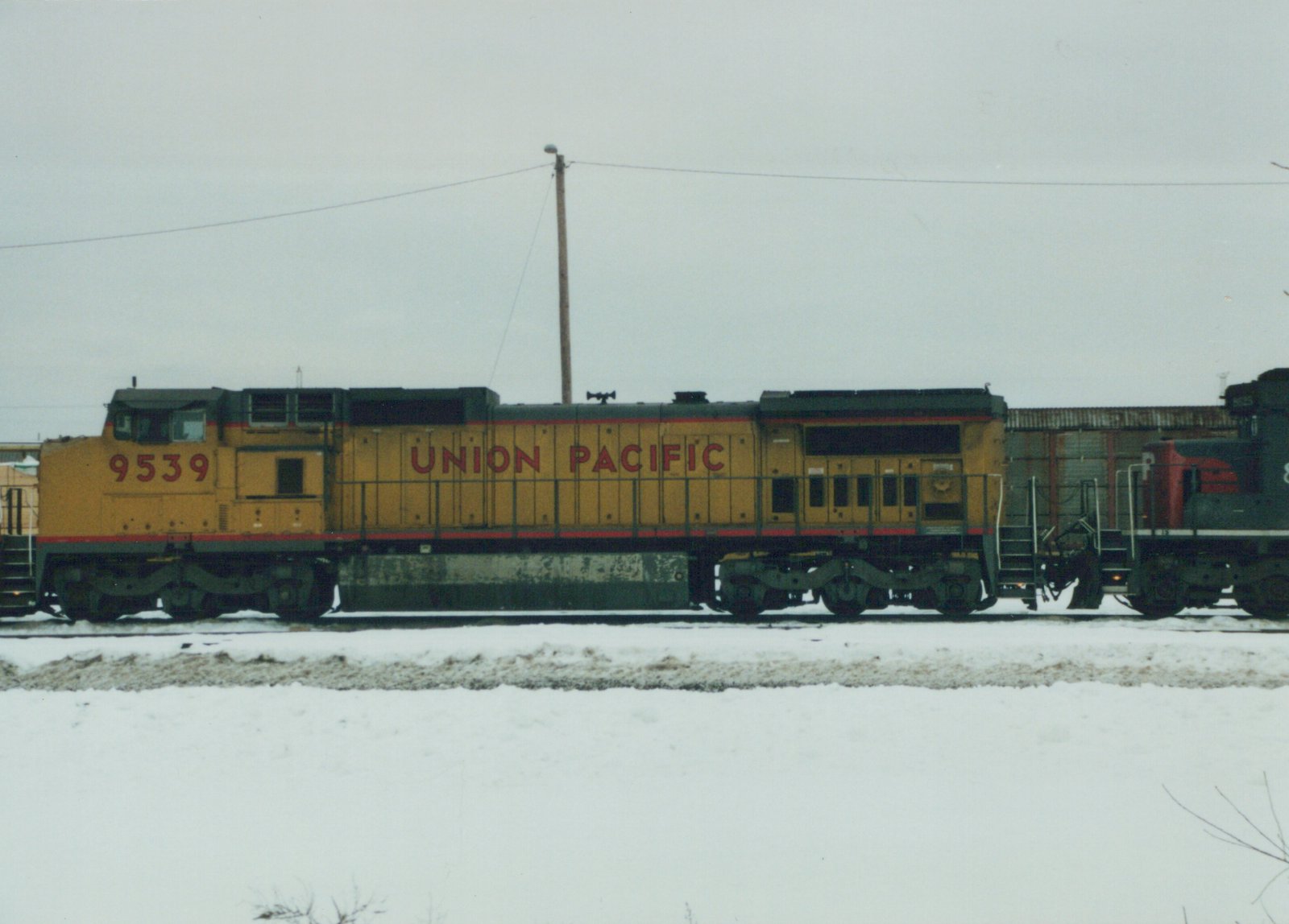 A yellow and red Union Pacific diesel locomotive numbered 9539 is shown in profile on a snowy railroad yard, with a second locomotive partially visible behind it.