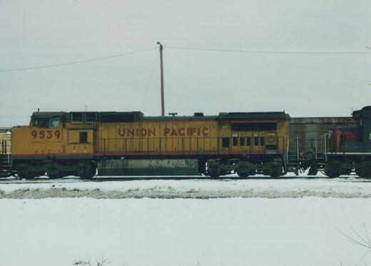 A yellow and red Union Pacific diesel locomotive numbered 9539 is shown in profile on a snowy railroad yard, with a second locomotive partially visible behind it.
