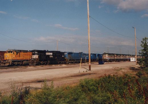 A photo showing multiple locomotives at a rail yard, including a yellow Union Pacific GP9, a black Norfolk Southern GP38-2, a blue locomotive, and an Amtrak F40PH in the background.
