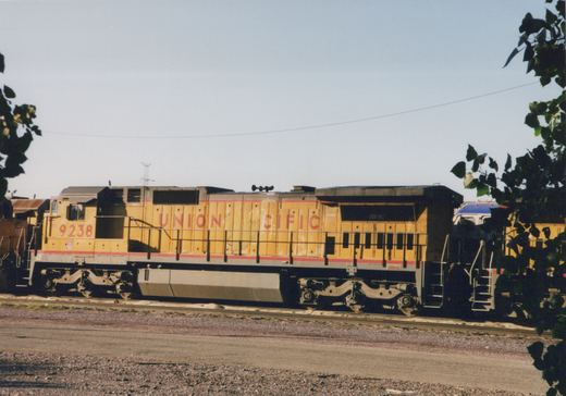 A yellow Union Pacific locomotive numbered 9238 is parked on tracks in a rail yard on a clear day, with trees framing the shot.