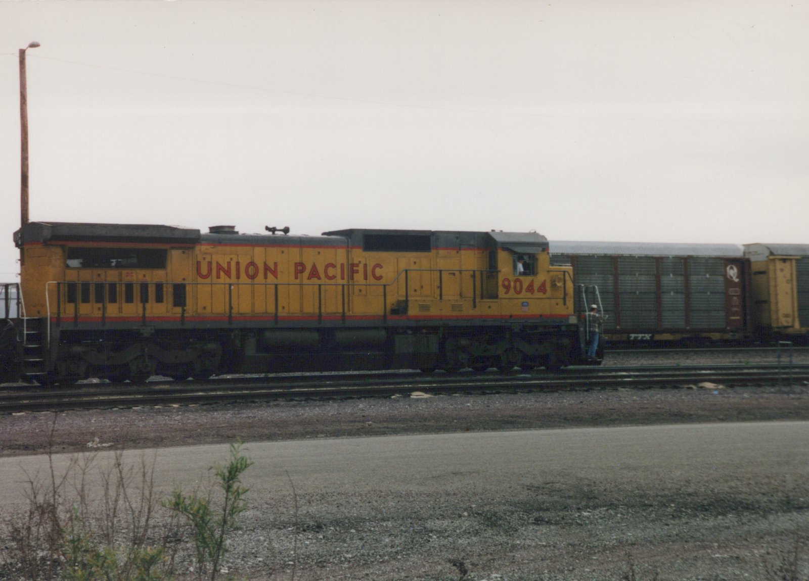 A yellow Union Pacific locomotive number 9044 sits on railroad tracks with a freight car behind it; two people are visible on the locomotive.