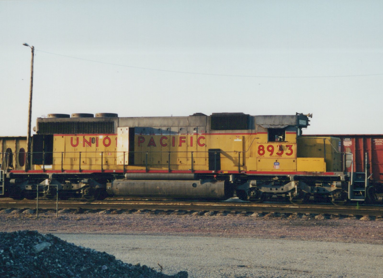 A yellow and red Union Pacific locomotive with the number 8933 on its side is parked on railroad tracks in a yard.