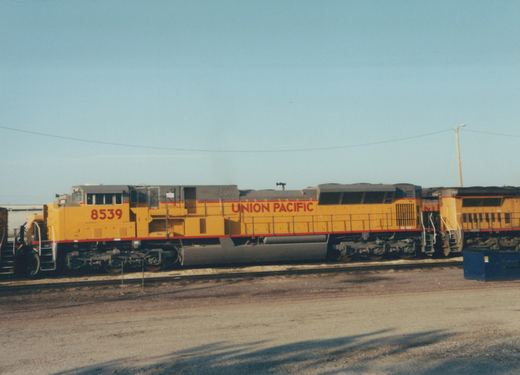 Two yellow Union Pacific diesel locomotives, 8539 and 9544, sit side-by-side on tracks in a gravel yard under a clear blue sky.
