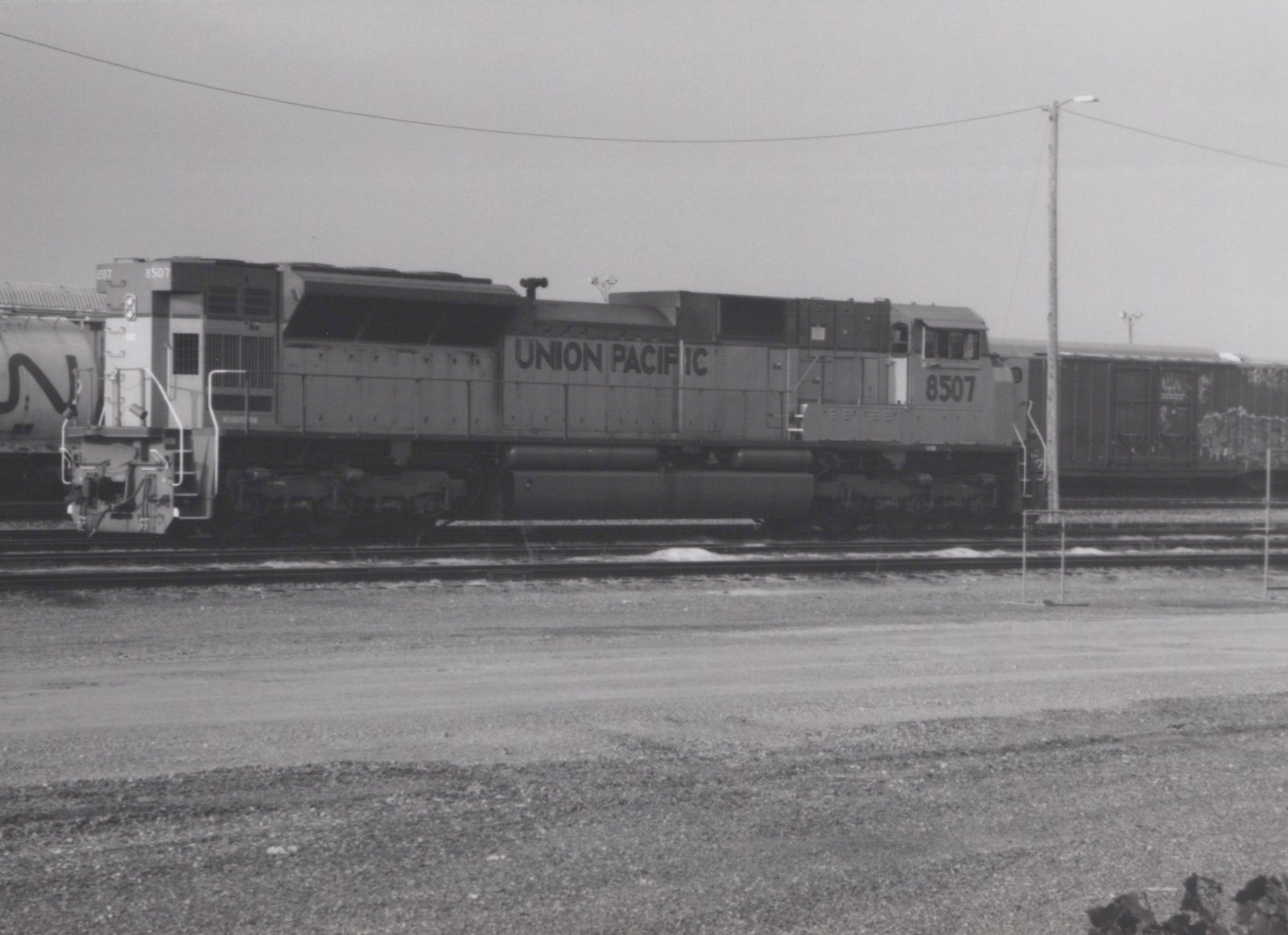 A black-and-white photo of a Union Pacific locomotive, number 8507, standing on tracks in a gravel yard with snow on the ground.