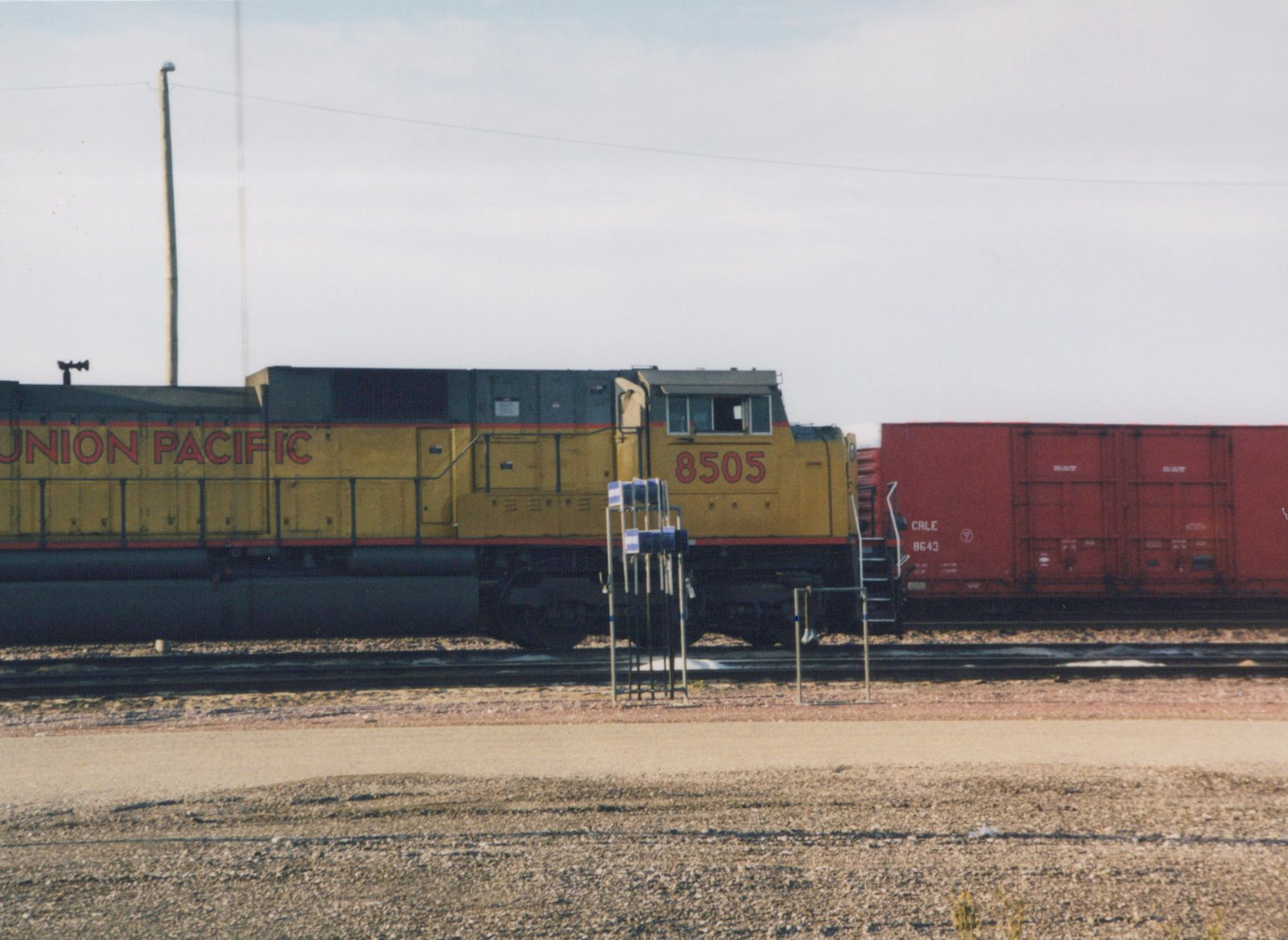 A yellow and red Union Pacific locomotive numbered 8505 stands on tracks beside a red boxcar numbered 8643, in what appears to be a rail yard.