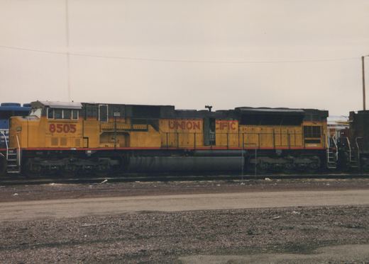 Side view of a yellow Union Pacific diesel locomotive, number 8505, parked on tracks in a gravel yard under a gray sky.