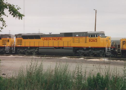 A yellow Union Pacific diesel locomotive numbered 8265 stands on tracks in a yard, with another locomotive visible behind it.