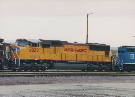 A side view of a yellow and black Union Pacific diesel locomotive with the number 4032, parked in a rail yard with other locomotives in the background.