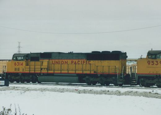 Two yellow and gray Union Pacific diesel locomotives, numbers 6314 and 9539, are parked on parallel tracks in a snow-covered yard under an overcast sky.