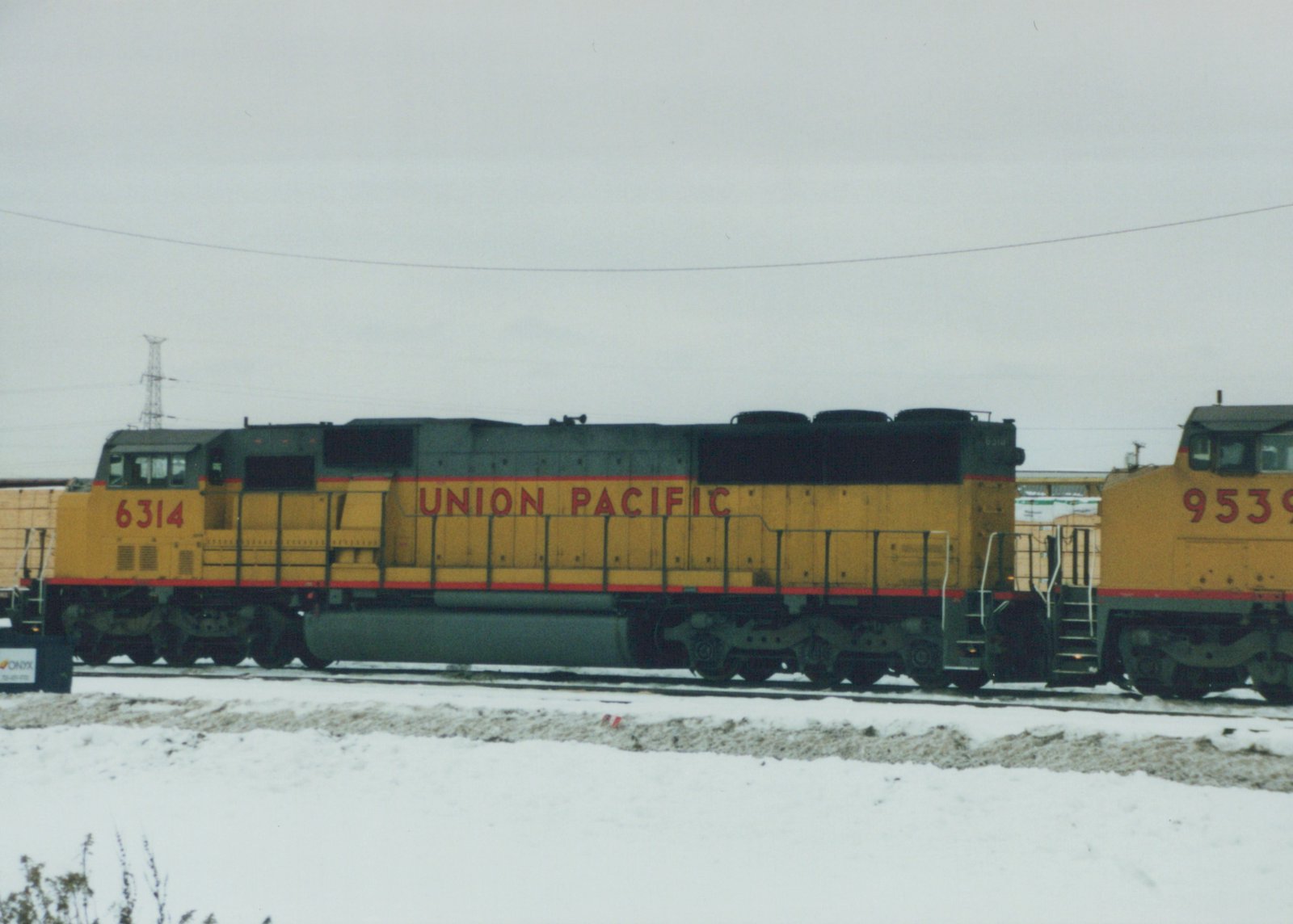 Two yellow and gray Union Pacific diesel locomotives, numbers 6314 and 9539, are parked on parallel tracks in a snow-covered yard under an overcast sky.