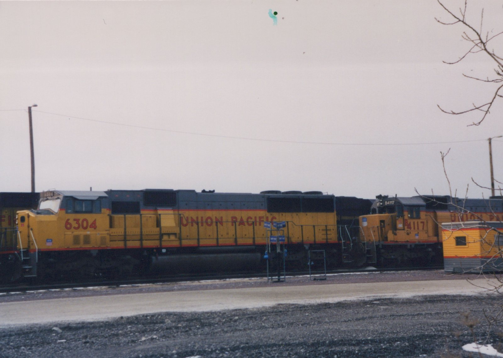 Side view of two yellow and gray Union Pacific diesel locomotives, numbered 6304 and 4117, standing on tracks in a yard with snow on the ground.