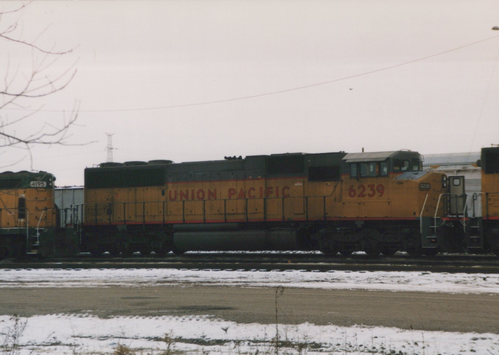 Side view of a yellow and black Union Pacific locomotive numbered 6239 standing on tracks in a snowy yard, with another similar locomotive partially visible behind it.