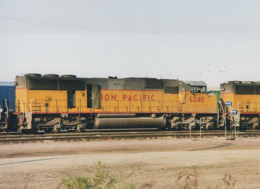 Two yellow and gray Union Pacific diesel locomotives, numbered 6240 and 6235, sit on parallel tracks in a gravel yard under a clear sky.