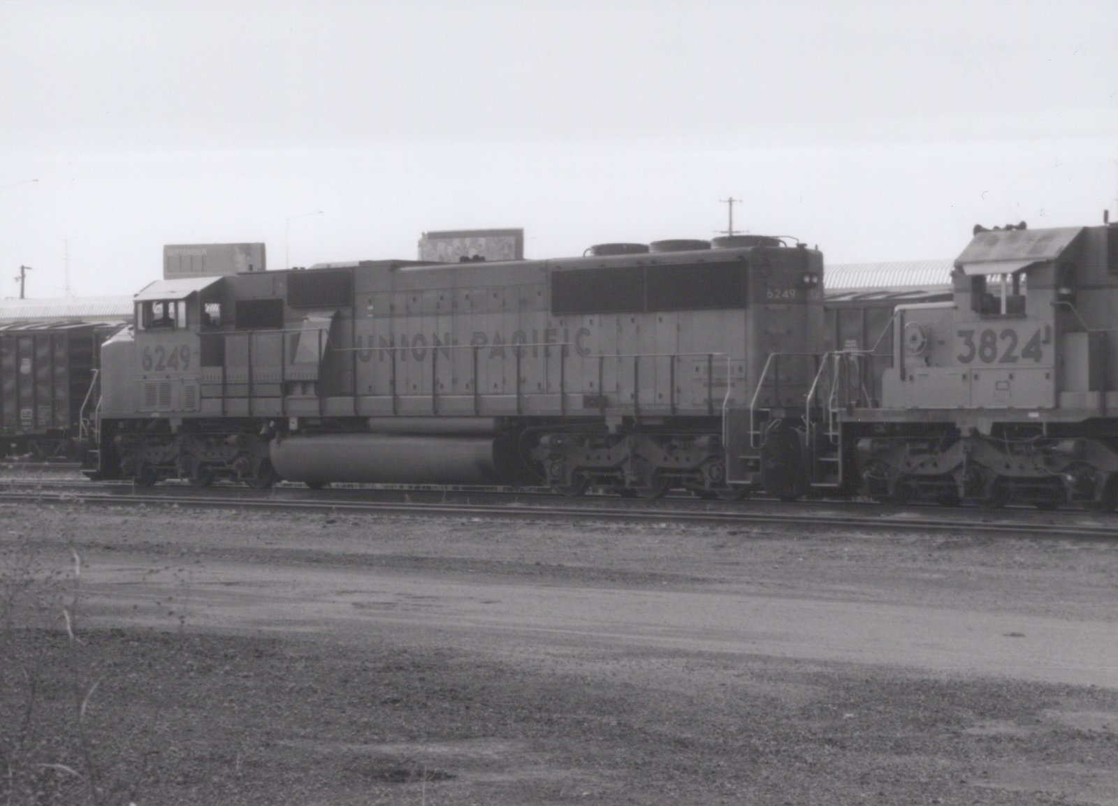 A black-and-white photo shows two Union Pacific diesel locomotives, numbered 6249 and 3824, side-by-side on tracks in a gravel yard under an overcast sky.