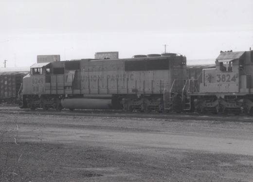 A black-and-white photo shows two Union Pacific diesel locomotives, numbered 6249 and 3824, side-by-side on tracks in a gravel yard under an overcast sky.