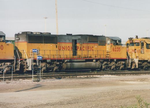 Side view of a yellow and gray Union Pacific SD40-2 locomotive, number 6235, parked on tracks in a railyard, with a second Union Pacific locomotive, number 9319, visible behind it.