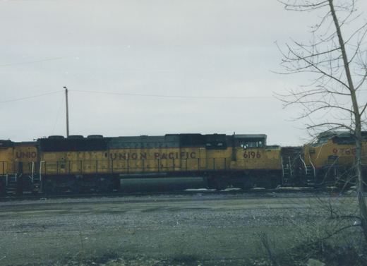 A side view of two yellow Union Pacific locomotives, numbered 6196 and 9768, parked in a gravel rail yard on a cloudy winter day.