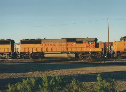Side view of a yellow and red Union Pacific diesel locomotive numbered 6040, parked in a rail yard with another locomotive partially visible behind it.