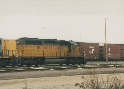 A yellow Union Pacific diesel locomotive with the number 5078 is parked on railroad tracks next to brown Conrail freight cars in a yard on a cloudy winter day.