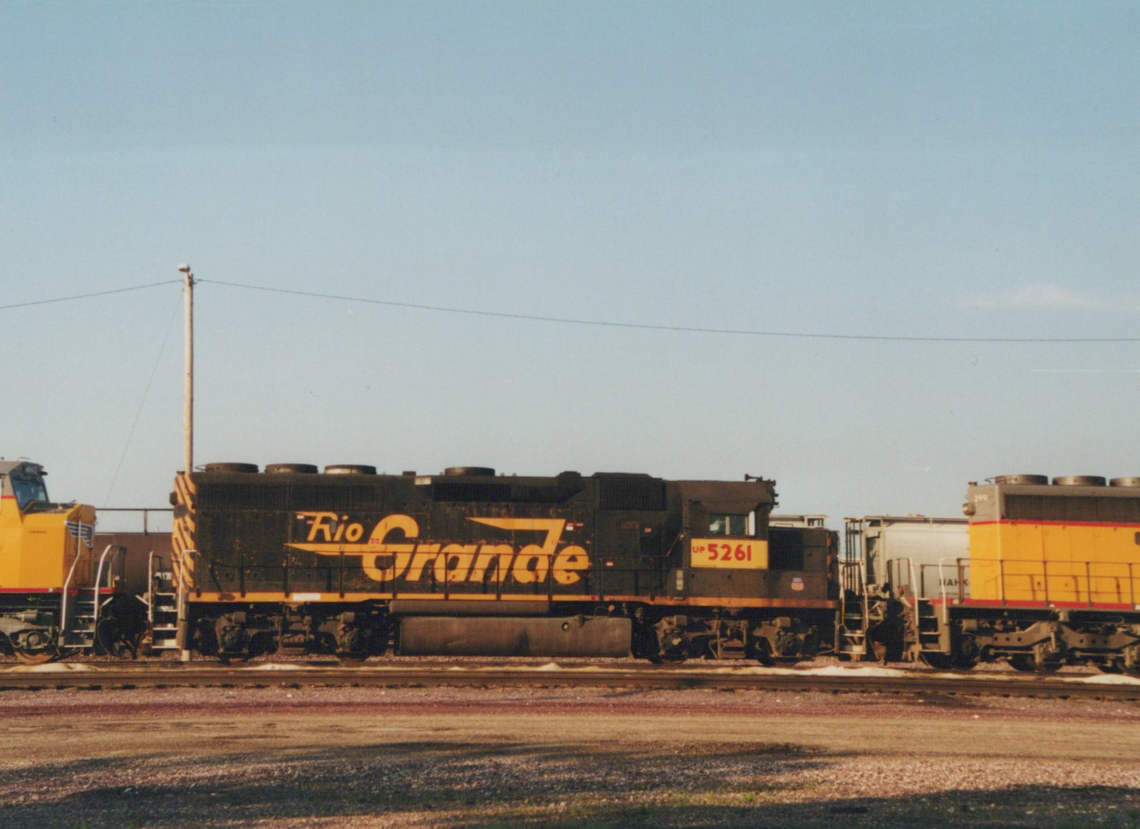 Two Union Pacific diesel locomotives are parked on parallel tracks in a sunny railyard; the front locomotive is black with yellow 'Rio Grande' lettering.