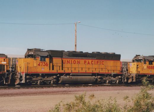 Two yellow Union Pacific locomotives, numbers 4736 and 9888, are parked side by side on railroad tracks in a gravel yard under a clear blue sky.