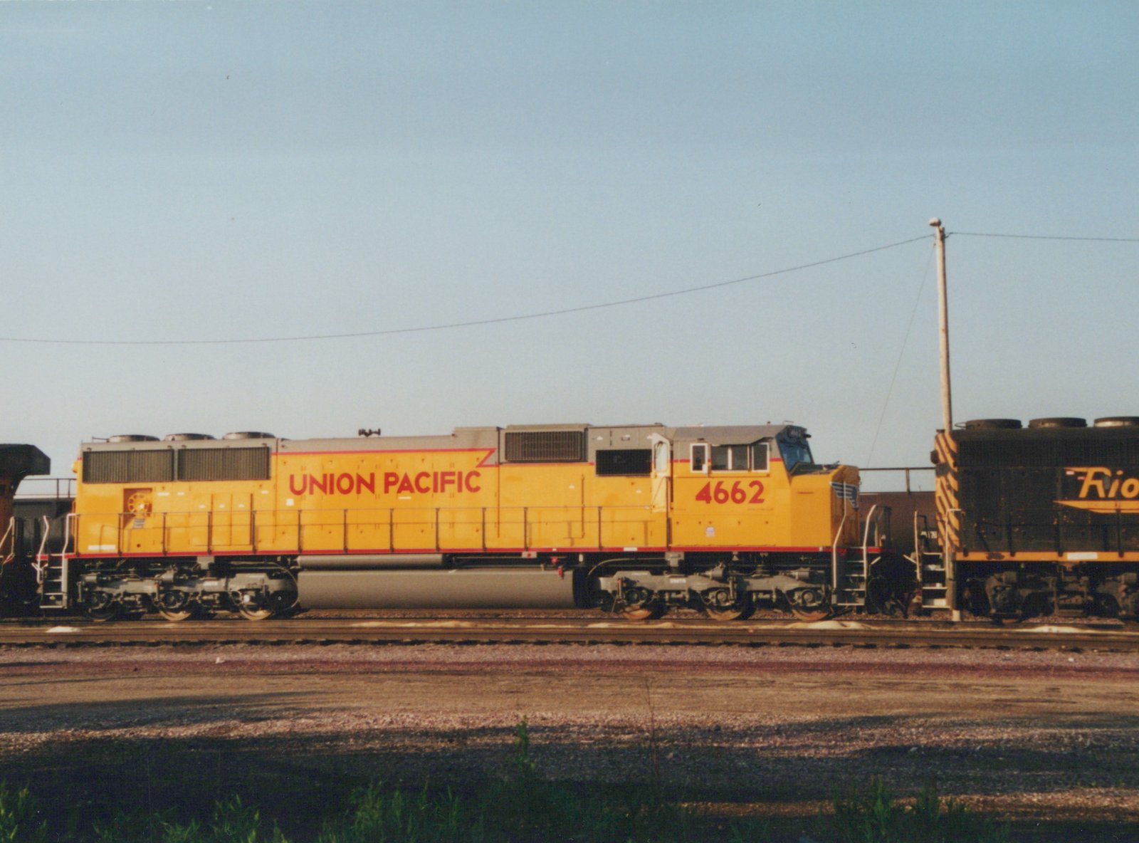 A yellow Union Pacific locomotive with the number 4662 on its side, standing on tracks in a yard with another black locomotive partially visible nearby.