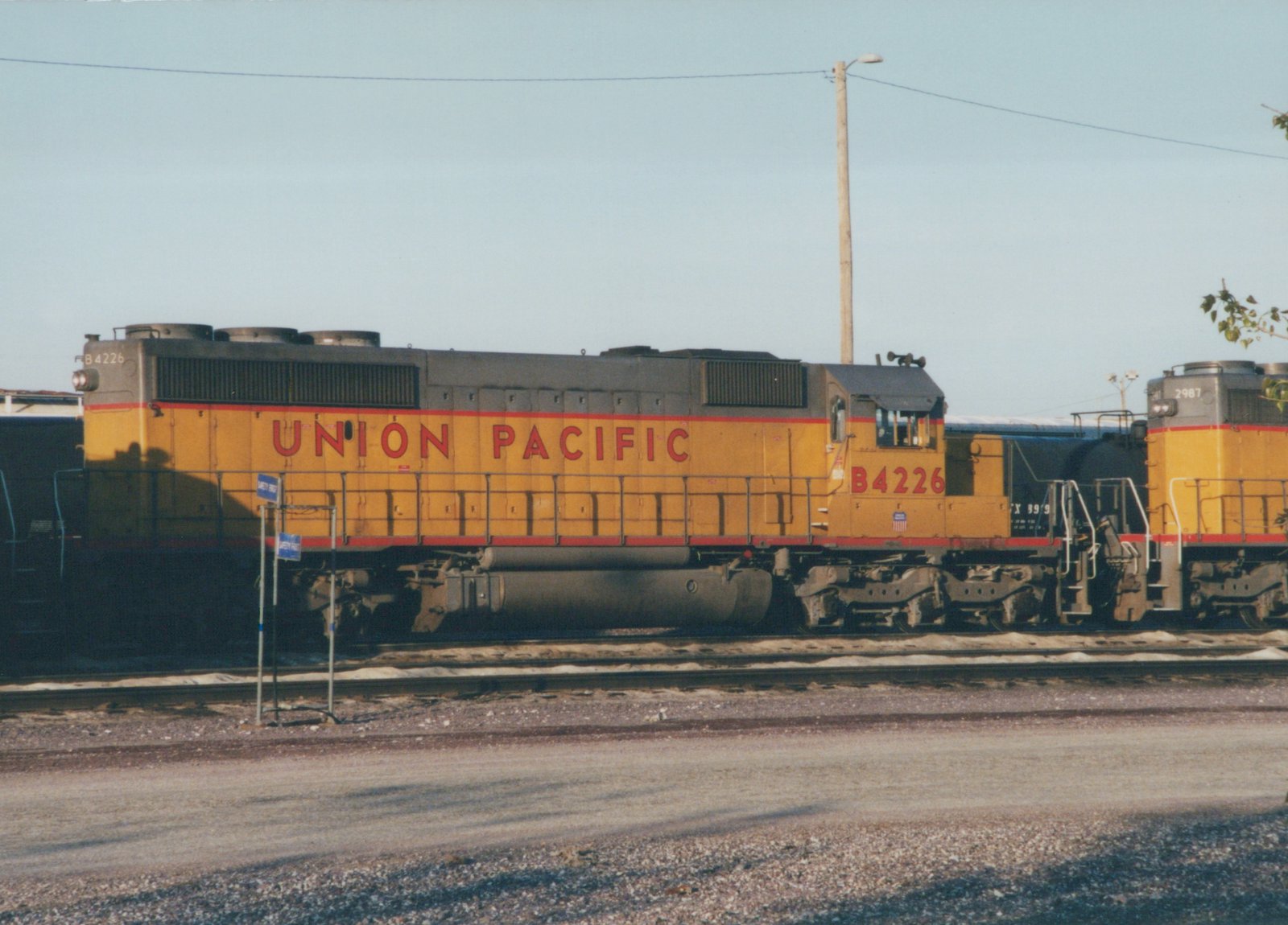 A yellow and gray Union Pacific diesel locomotive numbered B4226 seen from the side on a yard track, with a black tank car and another yellow locomotive numbered 2987 behind it.