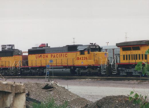 A yellow and gray Union Pacific diesel locomotive numbered B4226, coupled between two other yellow locomotives on a yard track, with a rubble pile and gravel in the foreground and an overcast sky.