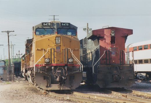 Two yellow and red Union Pacific diesel locomotives face the camera on parallel tracks in a railroad yard under a clear sky.