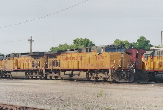 A side view of several yellow Union Pacific diesel locomotives with red lettering, parked in a gravel yard on a cloudy day.