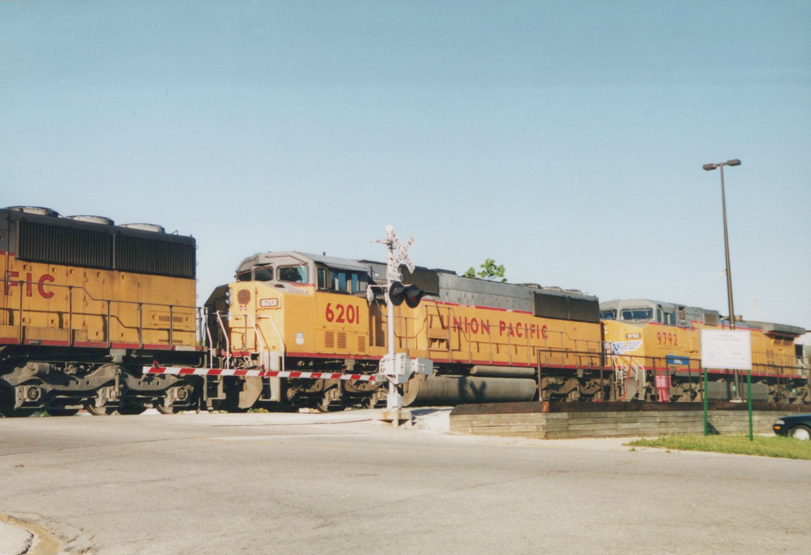 A yellow Union Pacific locomotive numbered 6201 crosses a street at a railroad crossing, with a second locomotive, 9792, following behind under a clear blue sky.