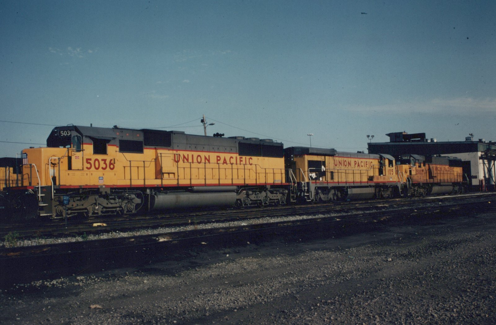 Three Union Pacific diesel locomotives, numbered 5036, 105, and 5003, side by side in a yard under a clear sky.