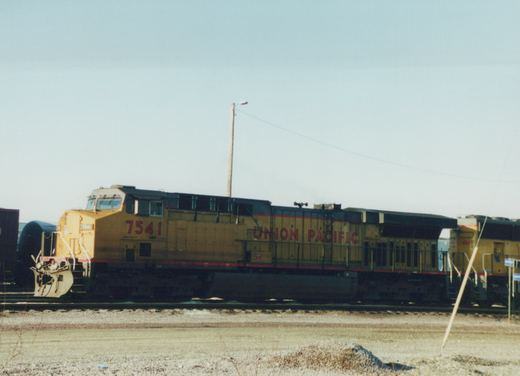 A yellow Union Pacific locomotive numbered 7541 stands on railroad tracks in a barren, wintry yard under a clear sky.