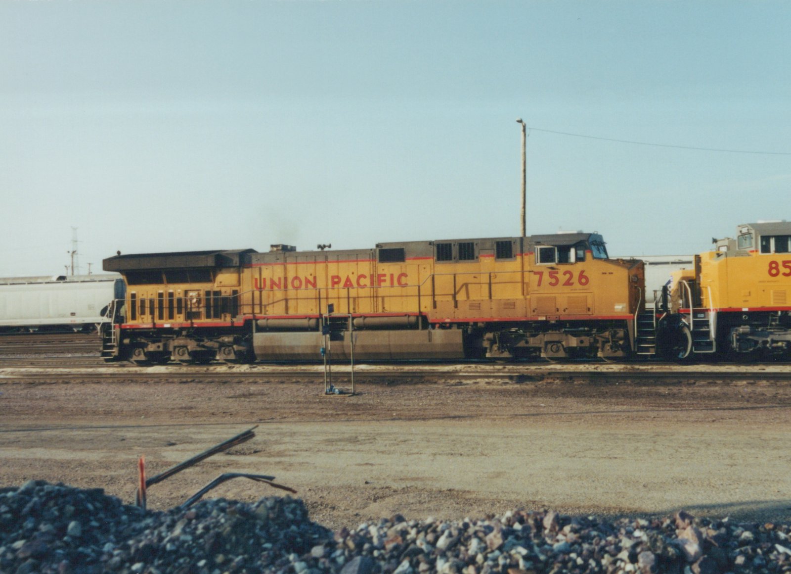 Two yellow Union Pacific diesel locomotives on tracks in a gravel yard under a clear sky.