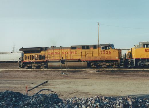 Two yellow Union Pacific diesel locomotives on tracks in a gravel yard under a clear sky.