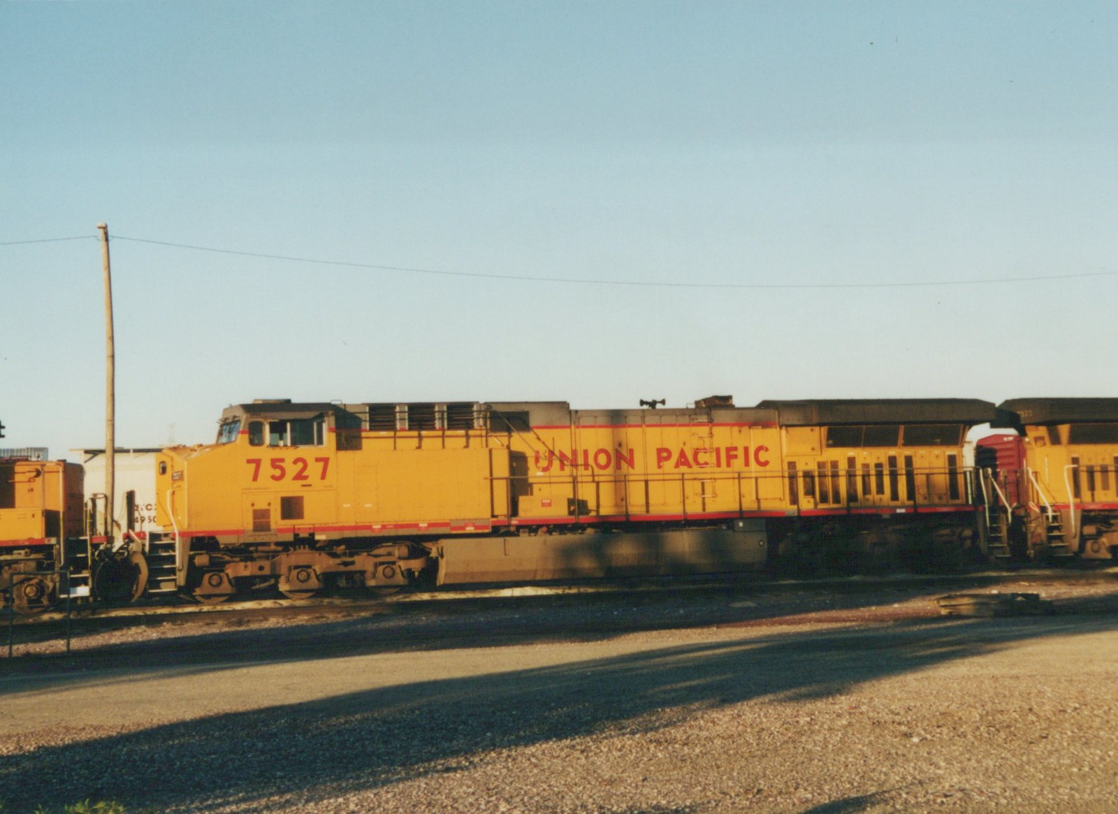 A yellow Union Pacific diesel locomotive with the number 7527 on its side, parked in a gravel yard under a clear sky.