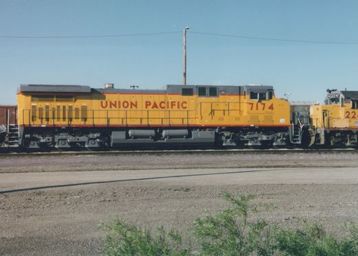 Side view of two yellow Union Pacific diesel locomotives, numbers 7174 and 2247, parked side by side on tracks in a gravel yard with a clear blue sky.