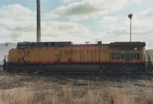 Side view of a yellow Union Pacific diesel locomotive, number 7170, parked in a yard with dry grass and an overcast sky.