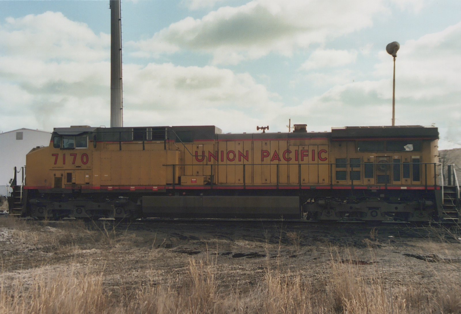 Side view of a yellow Union Pacific diesel locomotive, number 7170, parked in a yard with dry grass and an overcast sky.