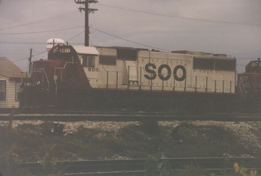 A side view of SOO Line locomotive 6011, an EMD SD40, on a railroad main line in Franklin Park, Illinois, with a water tower in the background.