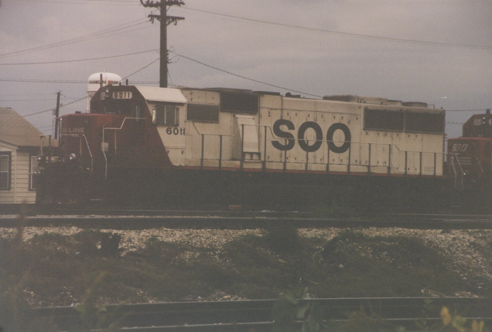 A side view of SOO Line locomotive 6011, an EMD SD40, on a railroad main line in Franklin Park, Illinois, with a water tower in the background.