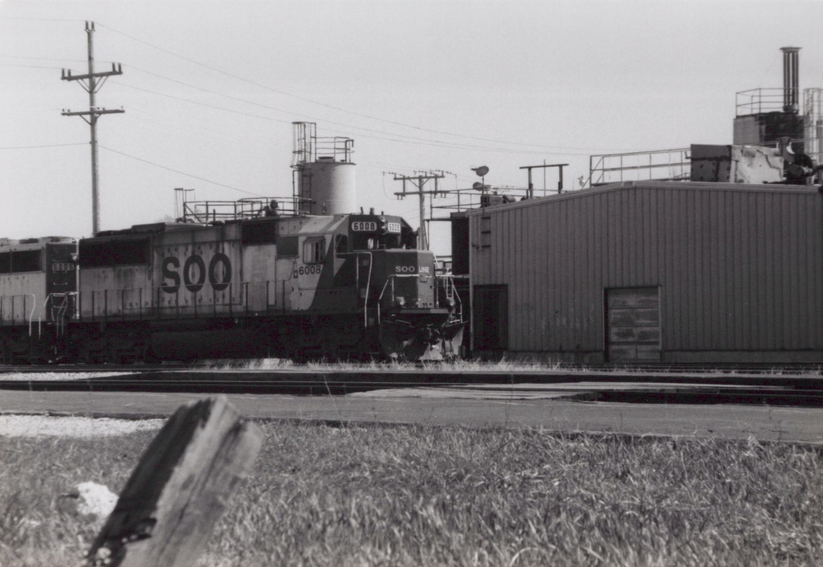 A black and white photograph of two SOO Line diesel locomotives, 6008 and 6015, standing side by side in a rail yard on a cloudy day.