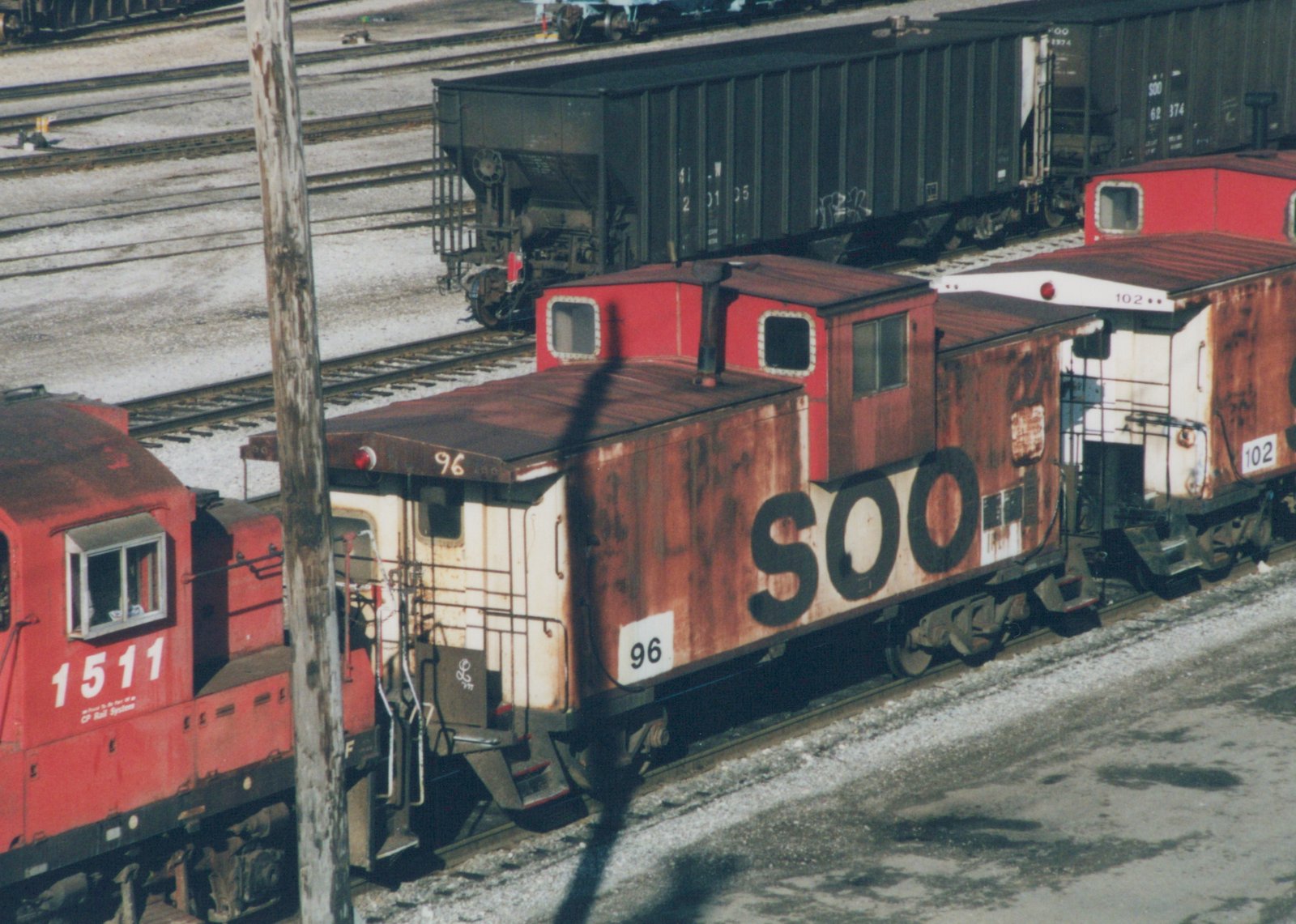 A red and white SOO Line caboose numbered 96 is parked on a railway track in a yard, with a red CP Rail locomotive numbered 1511 beside it.