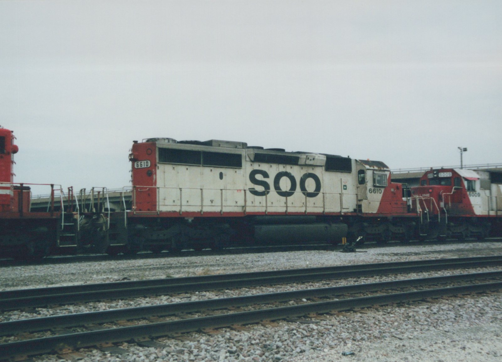 Two SOO Line diesel locomotives, 6610 and 6009, are coupled together on tracks in a gravel yard under an overcast sky.