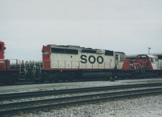 Two SOO Line diesel locomotives, 6610 and 6009, are coupled together on tracks in a gravel yard under an overcast sky.