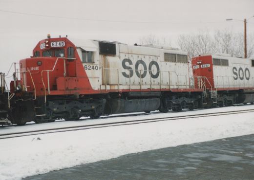 Two red and white diesel locomotives with 'SOO' lettering, numbered 6240 and 6241, are parked on snow-covered tracks on a cloudy day.