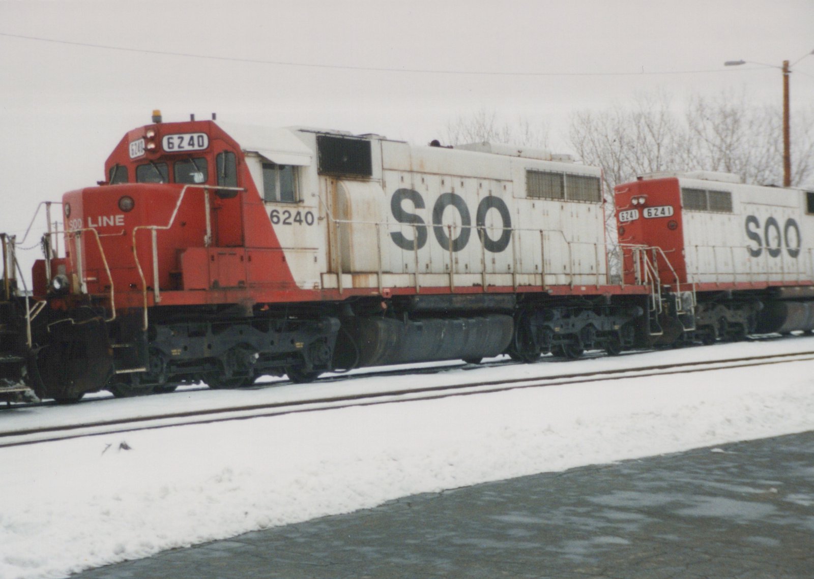 Two red and white diesel locomotives with 'SOO' lettering, numbered 6240 and 6241, are parked on snow-covered tracks on a cloudy day.