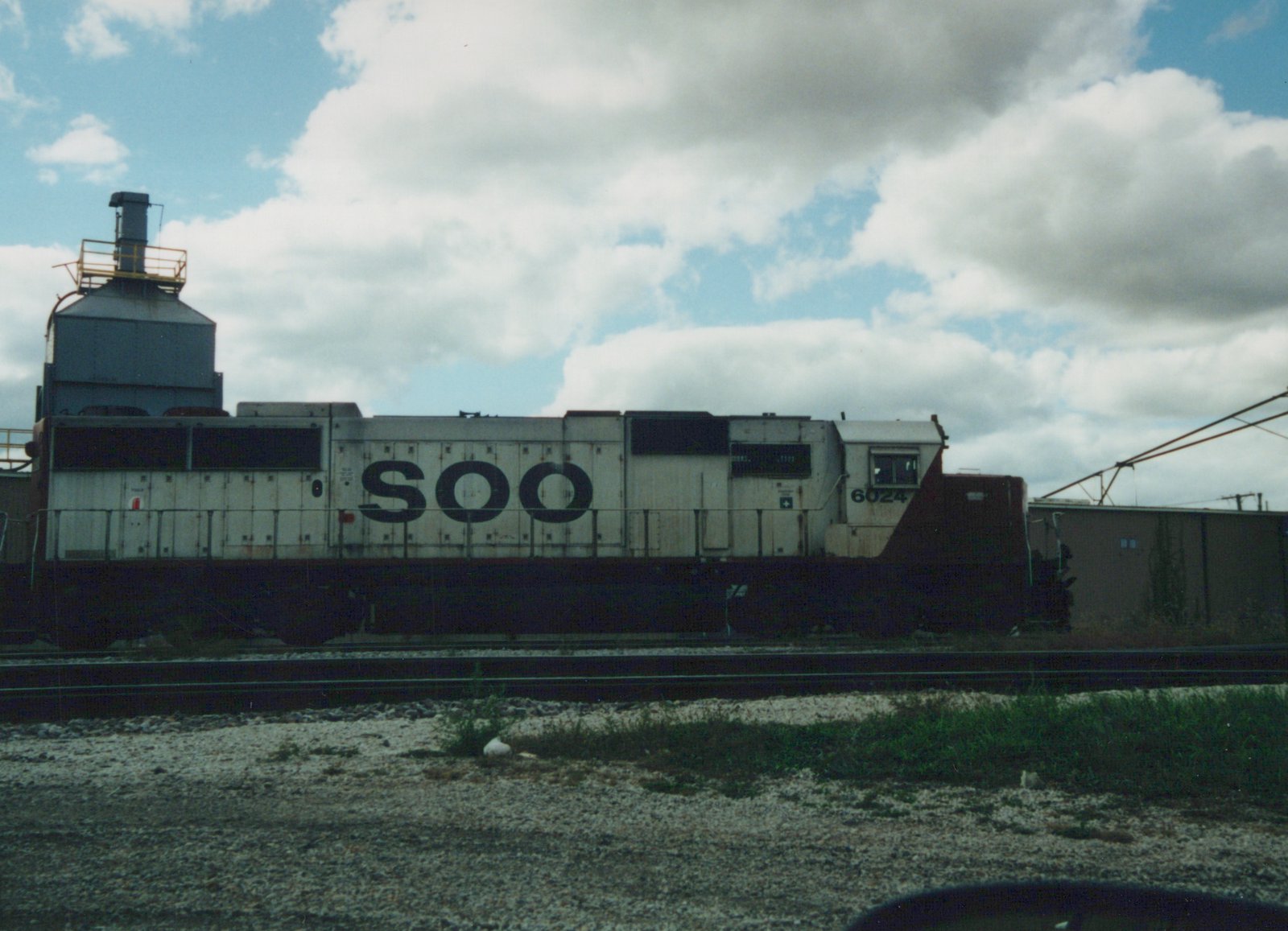A white and maroon SOO Line diesel locomotive with the number 6024 on the cab side, parked on railroad tracks in a yard.