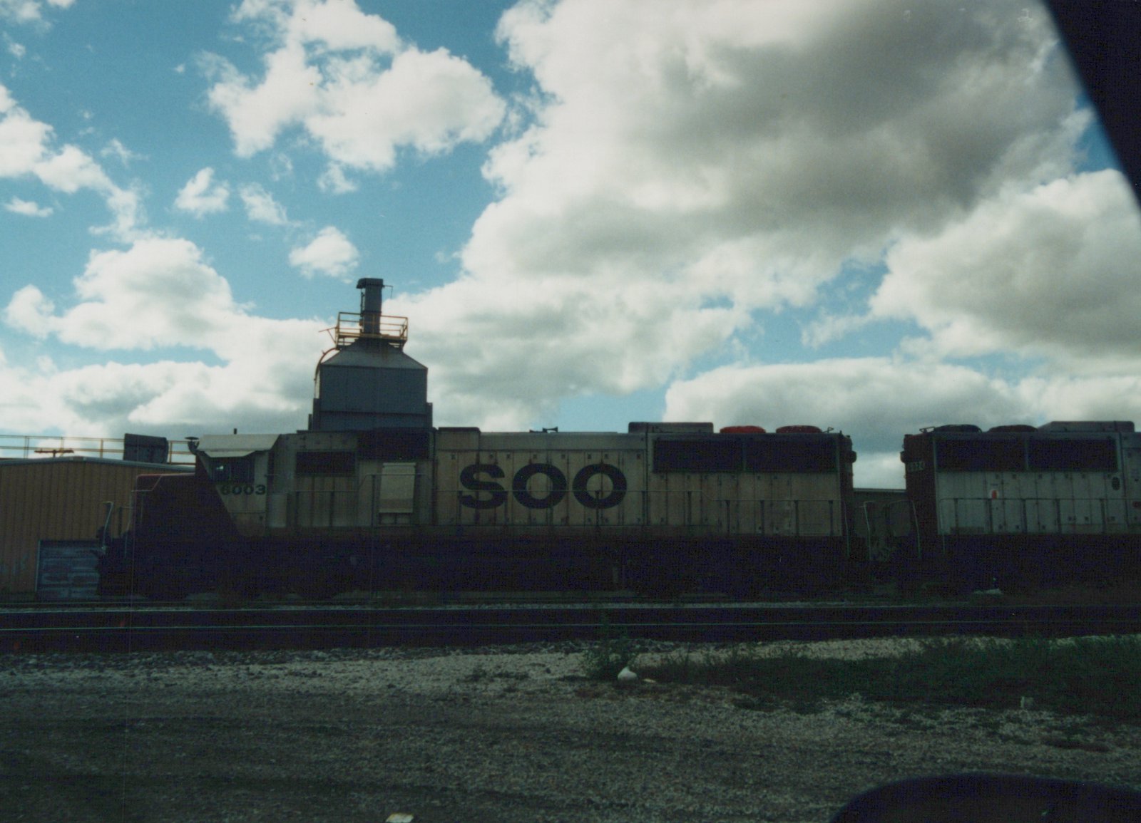 A side view of two SOO Line diesel locomotives, numbered 6003 and 6024, parked on parallel tracks in a gravel yard under a cloudy sky.